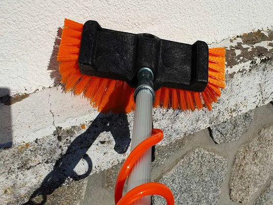 Nettoyage d'une façade en crépi encrassée de mousses et traces vertes avec une perche télescopique depuis le sol